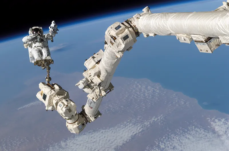 An astronaut riding on the end of the Canadarm2 robotic arm during a spacewalk.