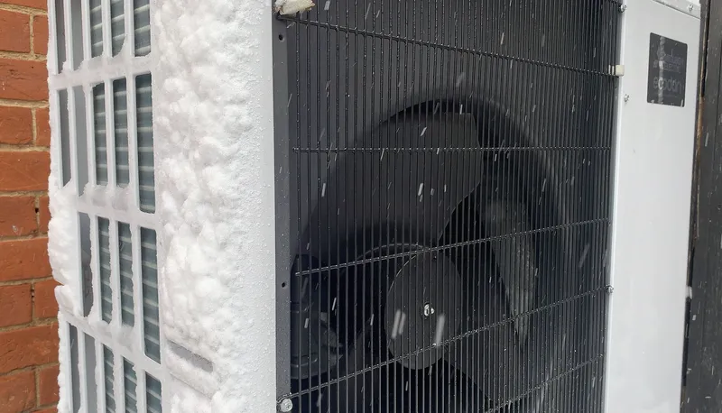 The outdoor unit of an air-source heat pump, still heating a home in the snow.