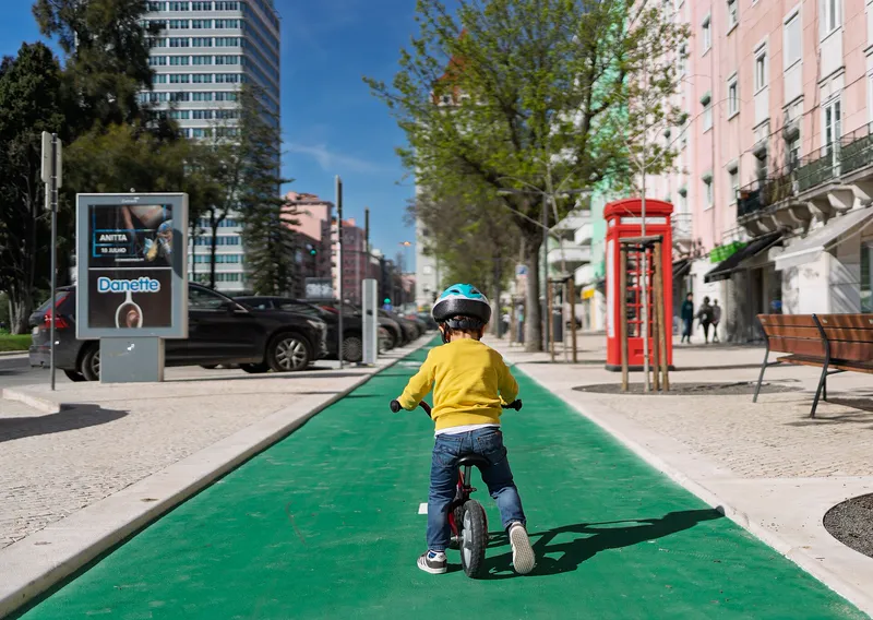 A child riding a balance bike on a separated cycle path in Lisbon.